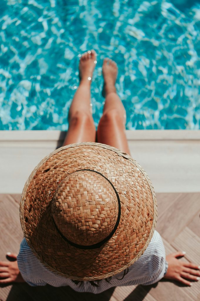 woman with toes in the pool wearing a sun hat